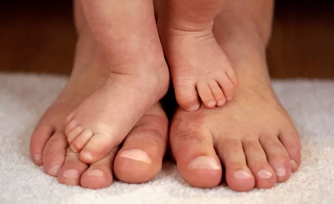 Babies' feet stand on adults' feet. Photo.